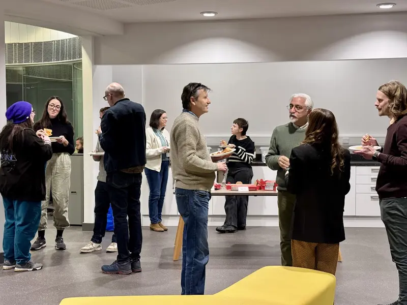 attendees stand and chat while in small groups while eating pizza at ding